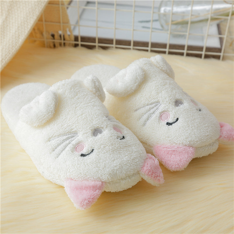 Pair of white plush slippers with pink accents on a wooden surface.