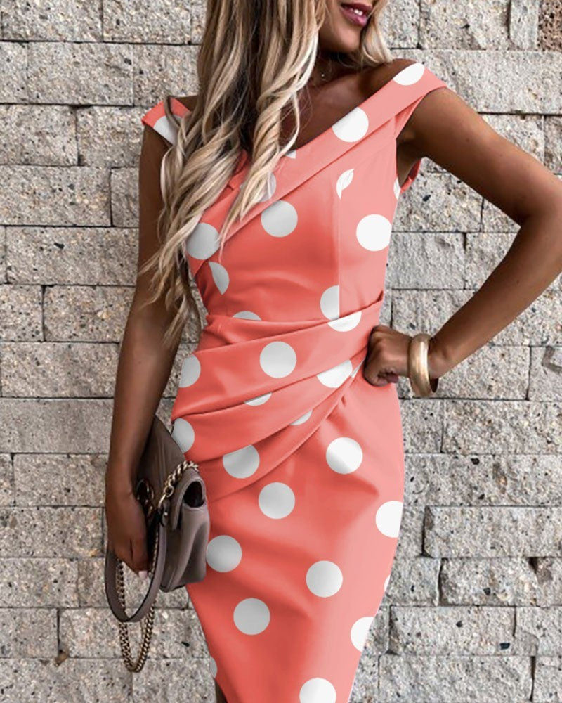 Woman wearing a coral dress with white polka dots against a stone wall.
