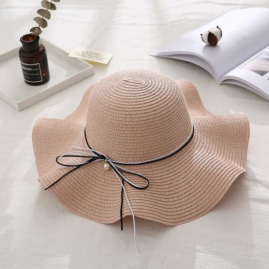 Beige straw hat with a black ribbon and pearl on a light surface.