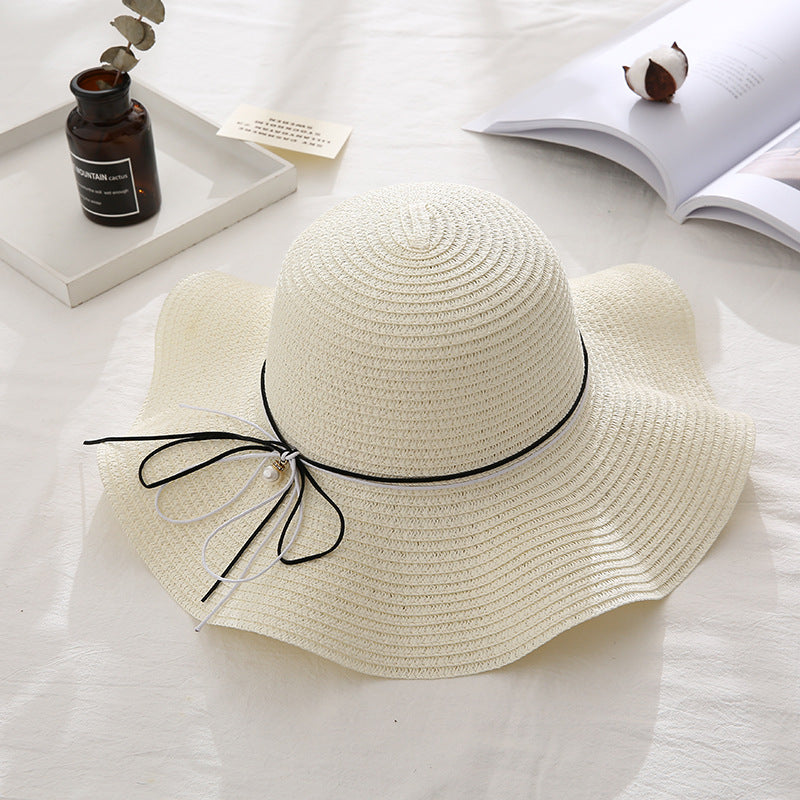 Beige straw hat with black ribbon on a light surface with books and a bottle.