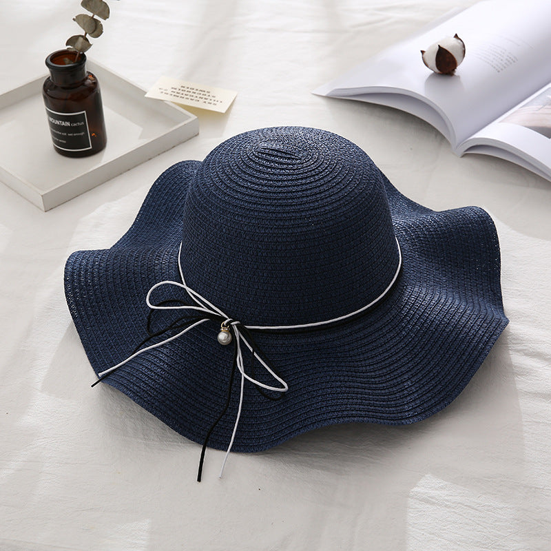 Navy blue straw hat with a white ribbon on a light surface.