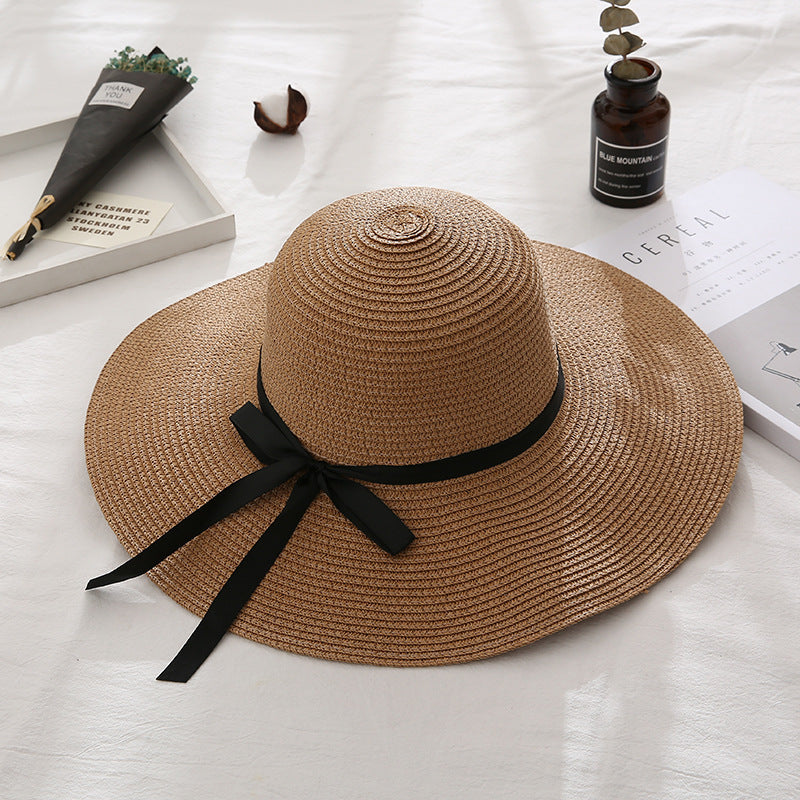Brown straw hat with a black ribbon on a light wooden surface.