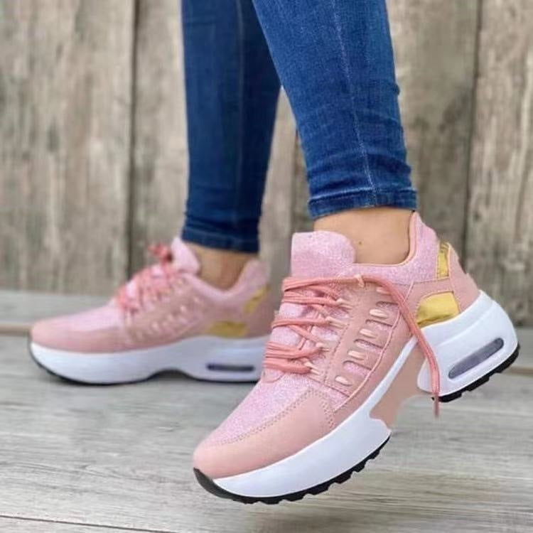 Pink sneakers with white soles worn by a person on a wooden floor.