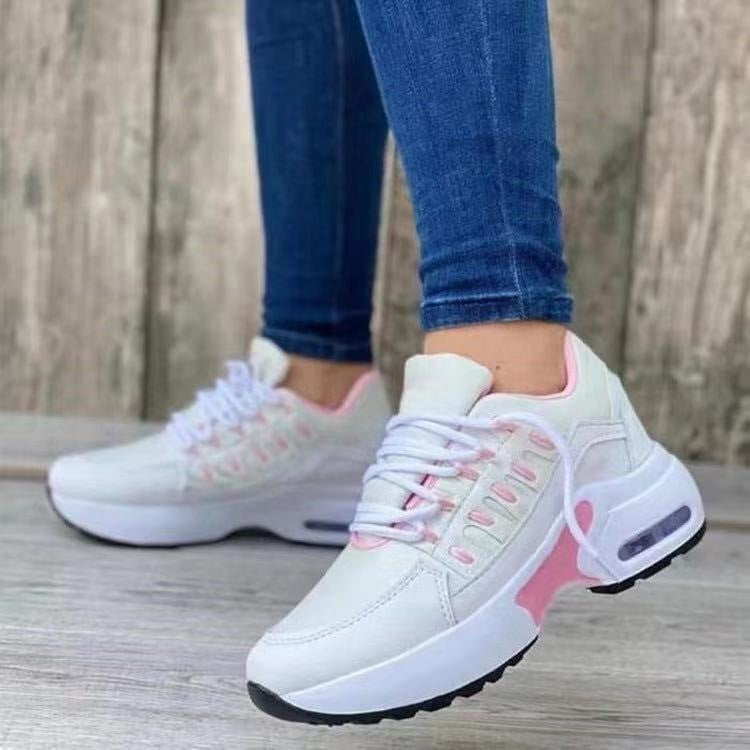 White sneakers with pink accents worn by a person on a wooden floor.