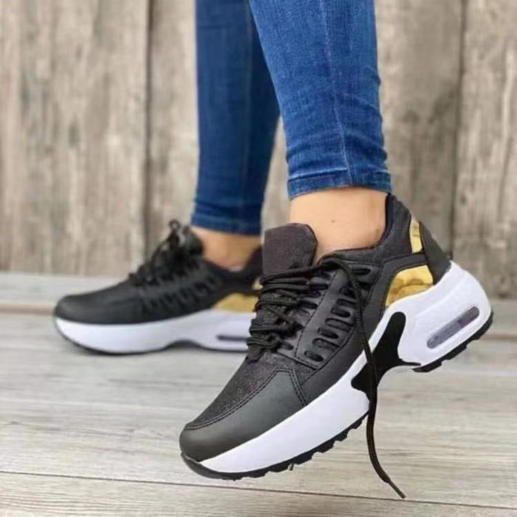 Black and gold sneakers worn with blue jeans on a wooden floor.