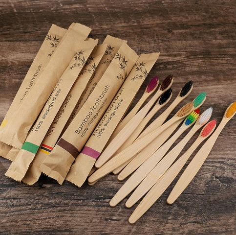 Set of bamboo toothbrushes with colored bristles and packaging on a wooden surface