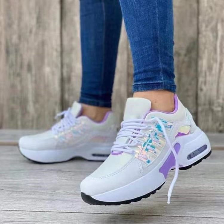 White sneakers with colorful accents worn with blue jeans on a wooden floor.