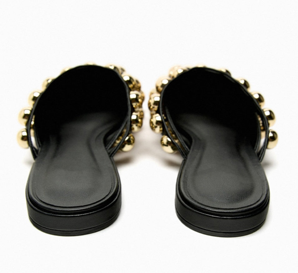 Black sandals with gold embellishments on a white background