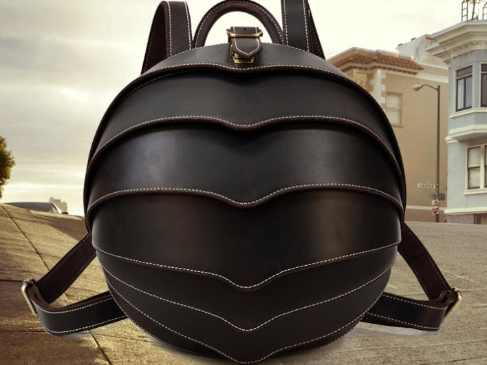 Stylish black leather backpack with beetle-inspired design on a city street – ideal for travel and daily use