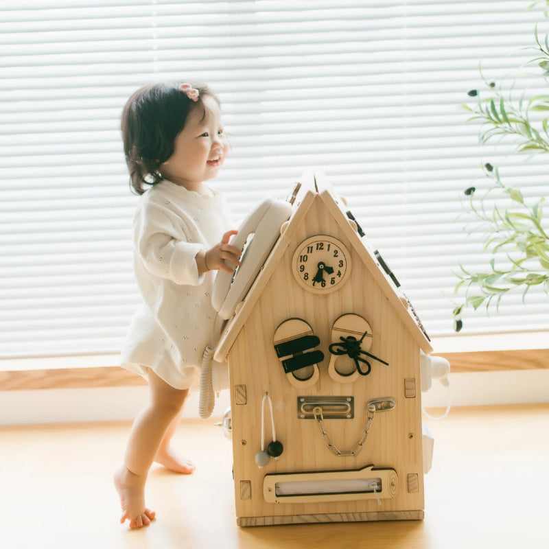 Child playing with a wooden toy telephone house in a bright room.