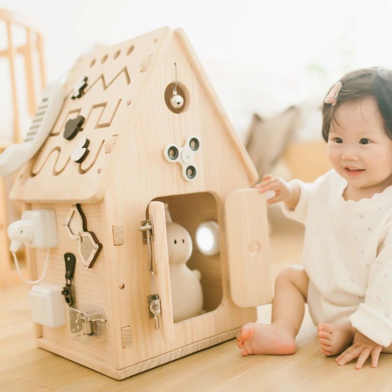 Child playing with a wooden toy house on a light wooden floor.