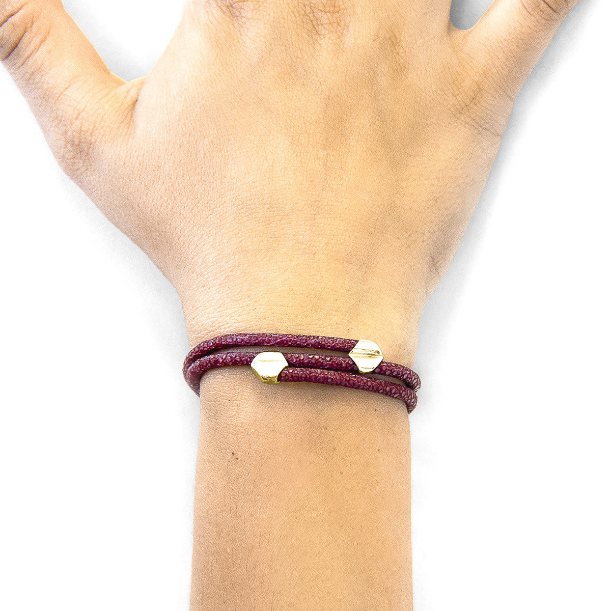 Hand wearing a burgundy bracelet with gold beads on a white background