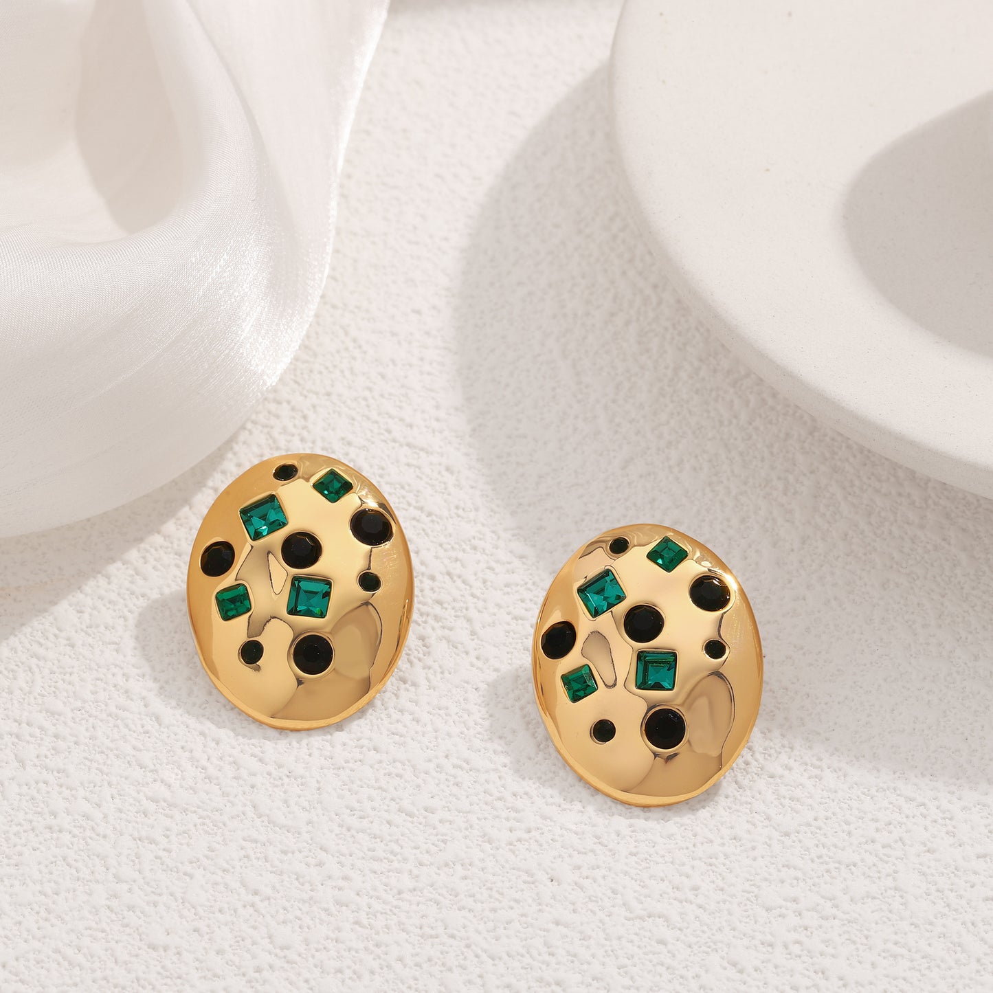 Gold earrings with green gemstones on a white surface