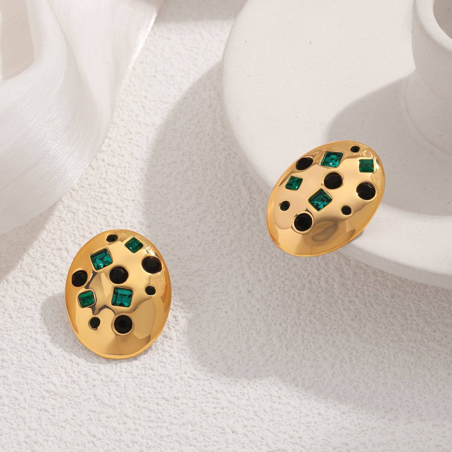 Gold earrings with green gemstones on a white fabric background