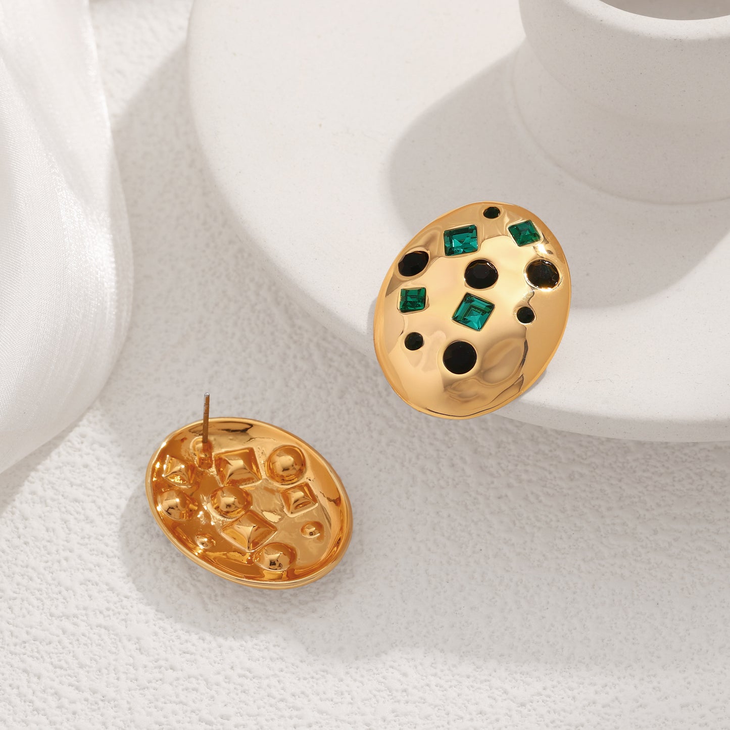 Gold earrings with green gemstones on a white surface
