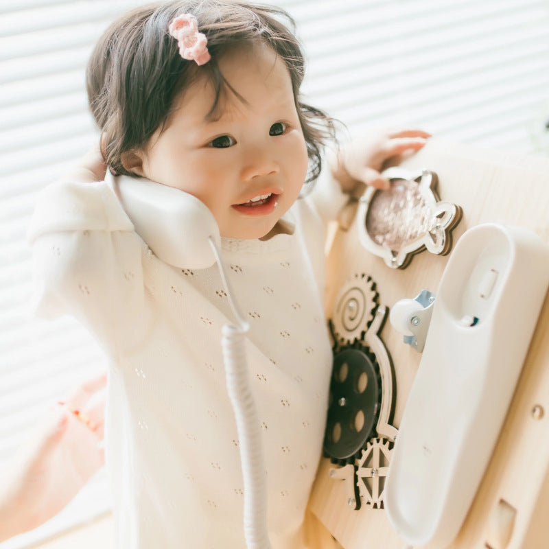 Child wearing a white outfit with decorative elements, sitting on a light-colored surface.