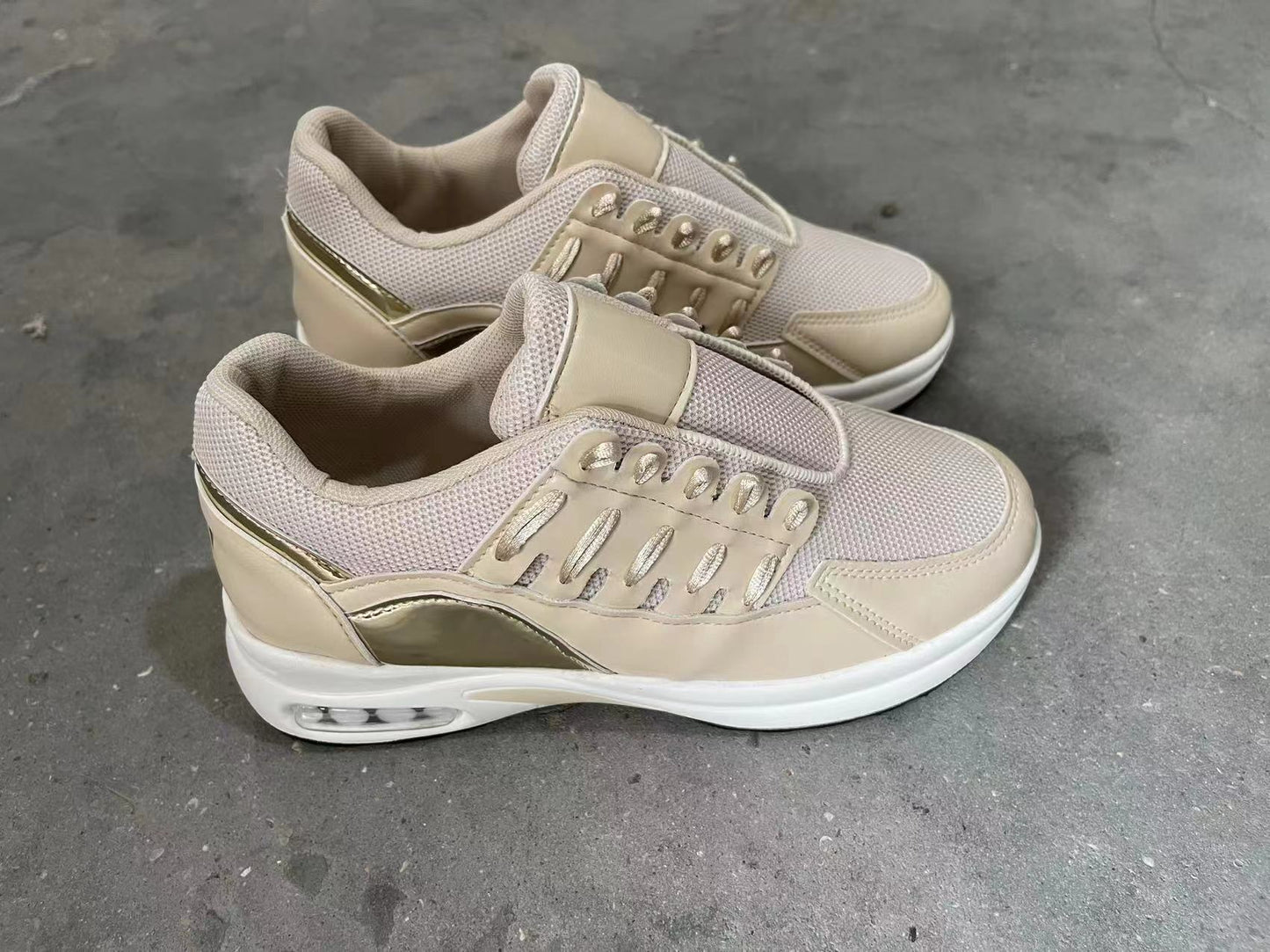 Beige sneakers with gold accents on a gray concrete floor