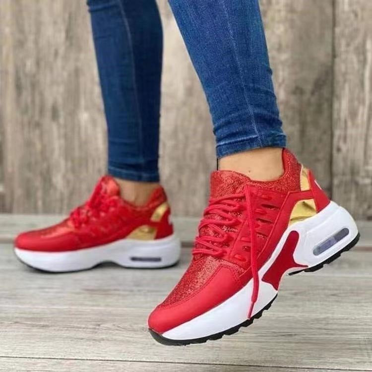 Red sneakers with gold accents worn by a person on a wooden floor.