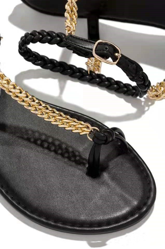 Black sandal with gold chain and black ankle strap on a white background