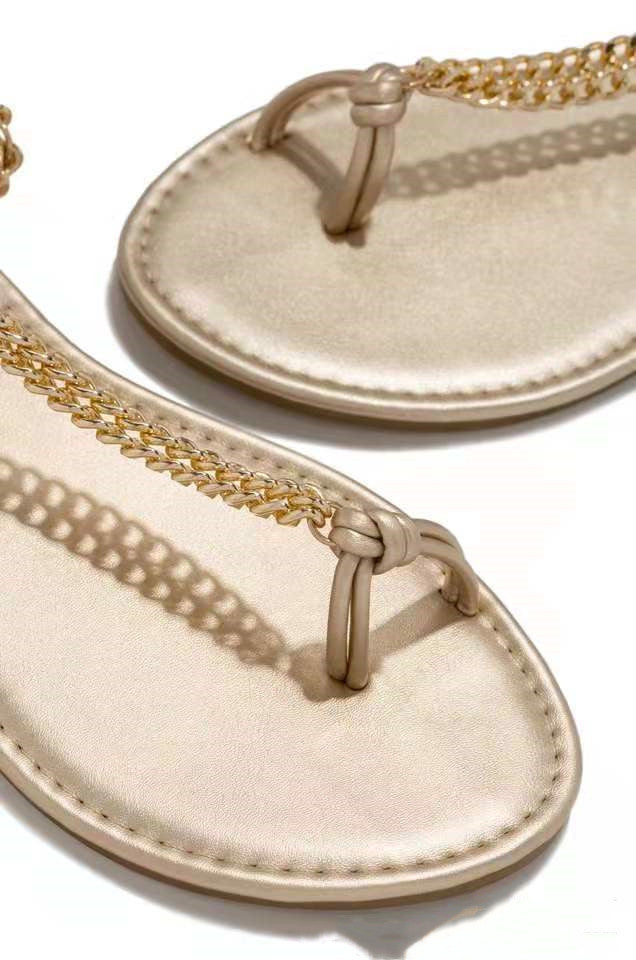 Beige sandals with gold chain details on a white background