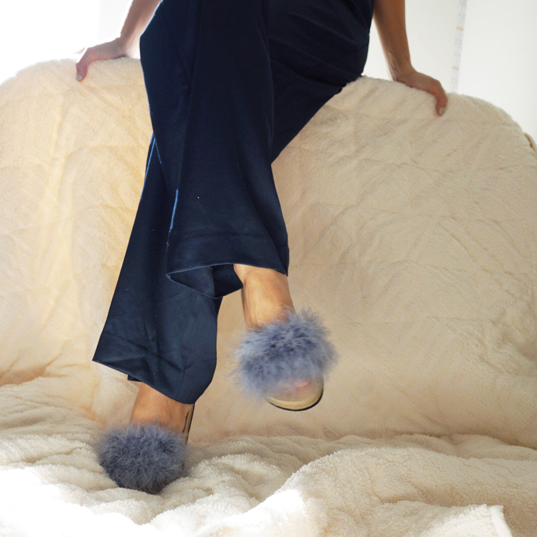 Person wearing dark pants and fluffy slippers on a beige surface
