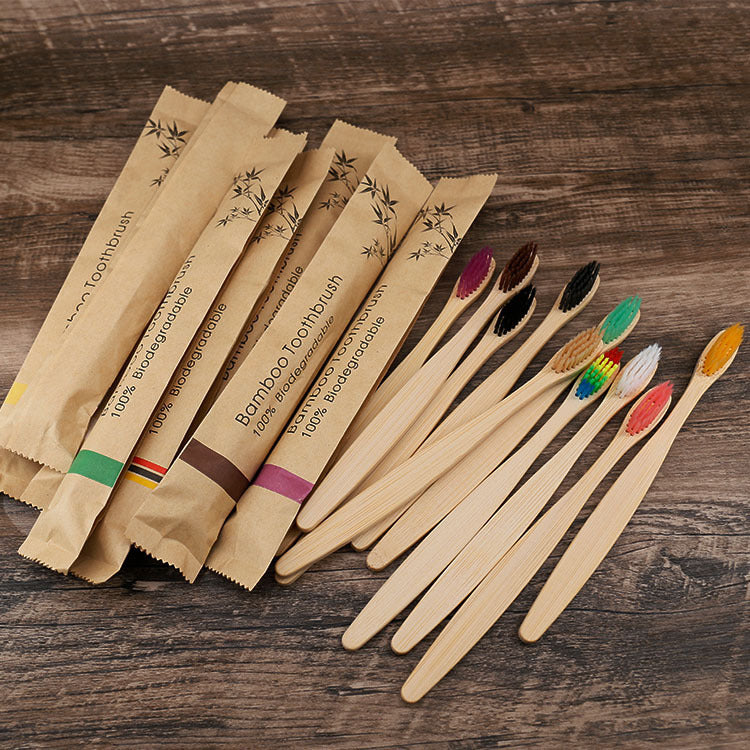 Set of eco-friendly bamboo toothbrushes with colorful soft bristles and individual kraft paper packaging, displayed on a brown background