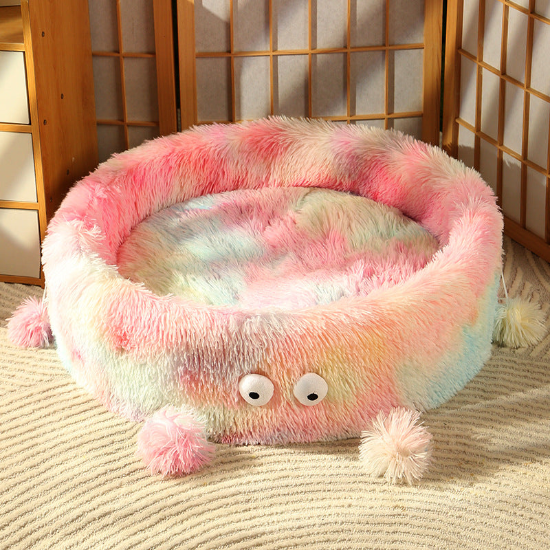 Fluffy pink and multicolored pet bed with googly eyes on a carpeted floor.