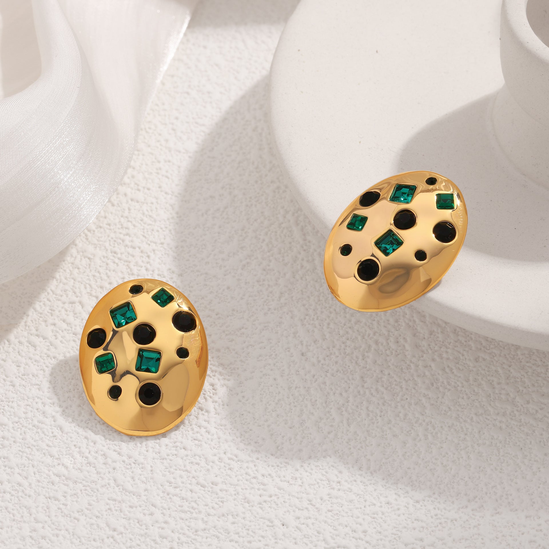 Gold earrings with green gemstones on a white fabric background