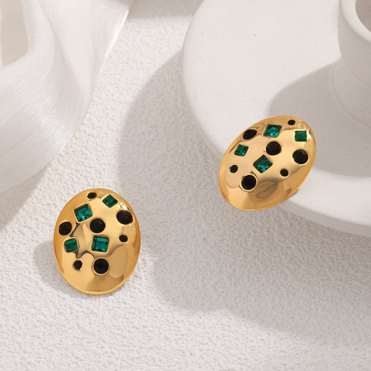 Gold earrings with green gemstones on a white fabric background