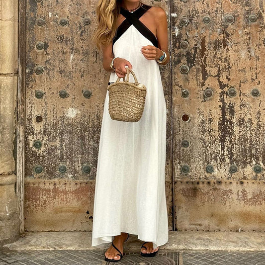 Woman in a white dress with black straps holding a woven bag against a textured wall.