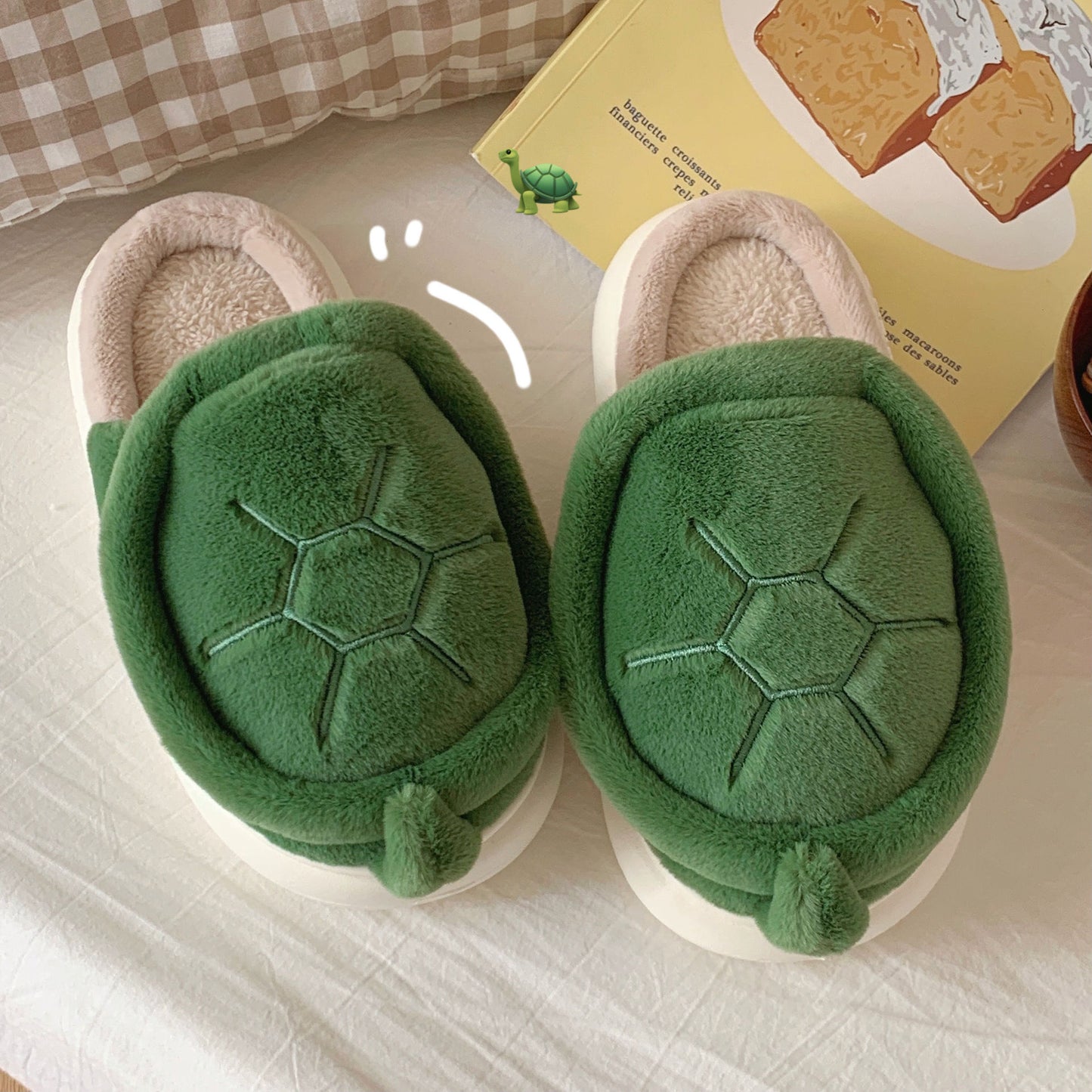 Green turtle-shaped slippers on a light surface with a book in the background