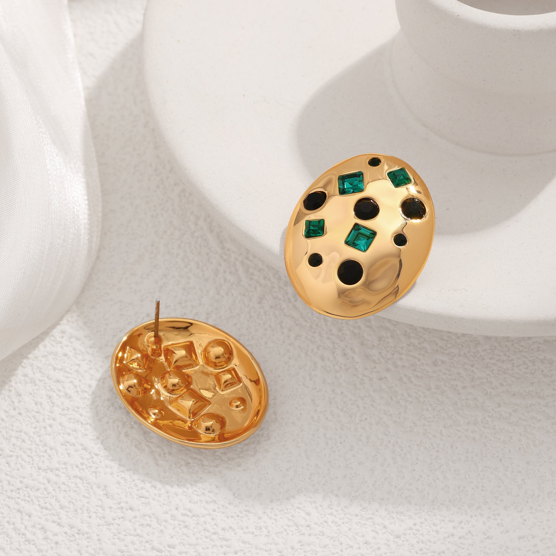 Gold earrings with green gemstones on a white surface