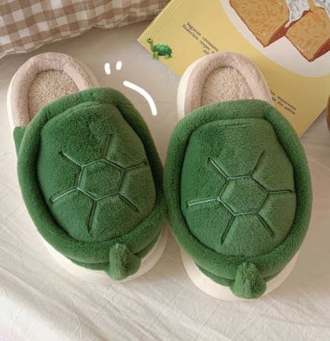 Green turtle-shaped slippers on a light surface with a book in the background.