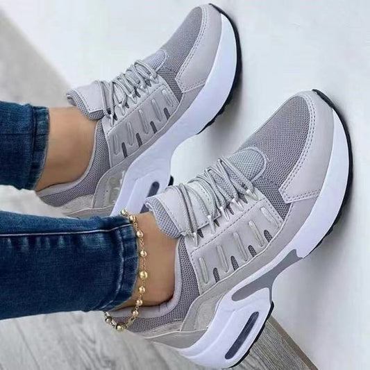 Light gray women's wedge sneakers with white soles, worn with jeans, resting against a light wall